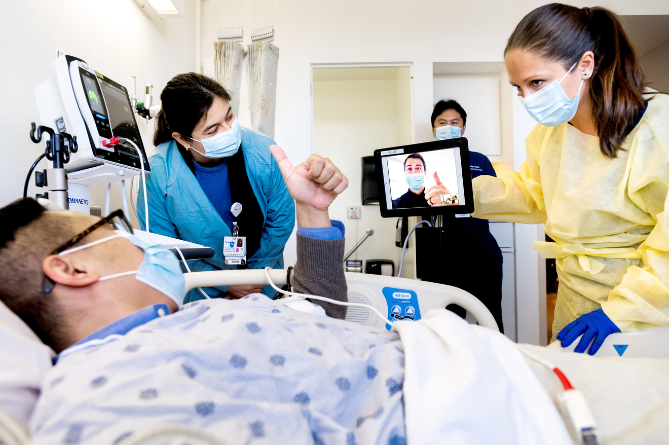Clinicians and patient in a bed using video conferencing